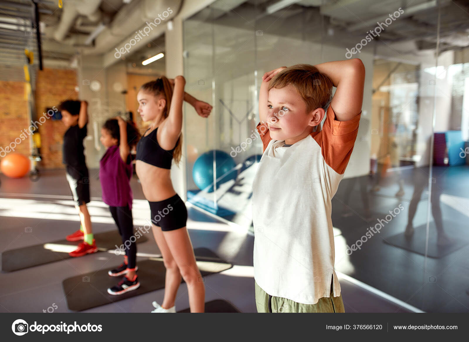 Be alive. Be strong. Be fit. Portrait of boy warming up exercising with other kids in gym. Stretching on a sunny day. Sport healthy lifestyle physical education concept Stock Photo