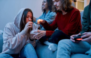 Marihuana içmek ve video oyunları oynamak. Genç adam, kız arkadaşı için marihuana ile nargile tüttürüyor, evde kanepede arkadaşlarıyla oturuyor ve dinleniyor.