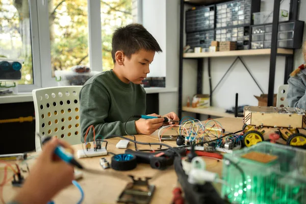 Leidenschaft, die Exzellenz schafft. Junge Ingenieurin mit Lötkolben, um Chips und Drähte zu verbinden. Robotik und Software Engineering für Grundschüler. Erfindungen und Kreativität für Kinder — Stockfoto