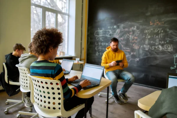 Educar a los estudiantes para el éxito en un mundo cambiante. Retrato de los alumnos que escuchan a su tutor, mientras están sentados con ordenadores portátiles durante una lección en la escuela inteligente moderna. Enfoque selectivo —  Fotos de Stock