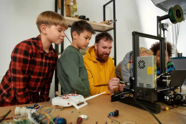 Τροφοδοτείται από την καινοτομία. Περίεργα παιδιά μαθαίνουν για την αρχή λειτουργίας του 3D εκτυπωτή από τον αρσενικό δάσκαλό τους στο μάθημα ρομποτικής — Φωτογραφία Αρχείου