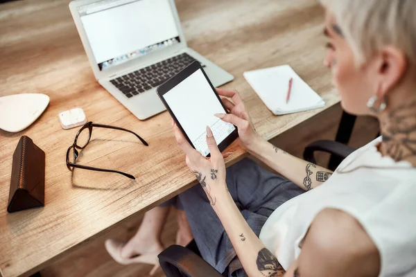 Τσεκάρω e-mail. Back view of young stylish blonde tattoomed business woman χρησιμοποιώντας το touchpad της ενώ κάθεται στο χώρο εργασίας της στο σύγχρονο γραφείο. Ψηφιακές τεχνολογίες στην εργασία — Φωτογραφία Αρχείου