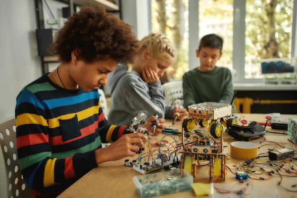 El poder de la inteligencia aplicada. Ingeniero joven usando soldador para unir chips y cables. Robótica e ingeniería de software para estudiantes de primaria. Invenciones y creatividad para niños — Foto de Stock