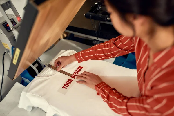 Személyre szabni. Vágott felvétel nő próbál, mozgó reklám matrica szöveggel, miközben készül nyomtatni egy póló — Stock Fotó
