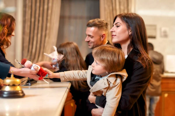 Dando una razón para sonreír. Happy family check in hotel en recepción. Recepcionista está dando un juguete para un niño mientras da la bienvenida a los huéspedes en el hotel . — Foto de Stock