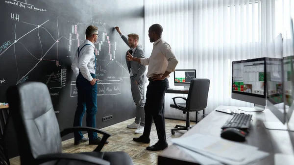 Tener profesores de nivel avanzado. De cuerpo entero de diversos empleados, comerciantes discutiendo la estrategia de trabajo, mientras que de pie cerca de pizarra llena de gráficos. Disparo horizontal —  Fotos de Stock