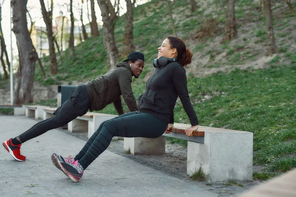 Пара тренирующихся в парке на улице. Активная атлетическая африканская пара отжимается на скамейке в парке. Упражнения вместе — стоковое фото