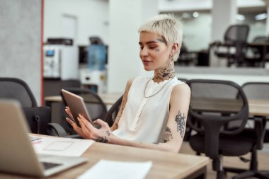 Meslektaşımla sohbet ediyorum. Genç ve çekici iş kadını dijital tablet kullanıyor ve iş yerinde otururken gülümsüyor. İş ve kariyer. Dijital teknolojiler iş başında