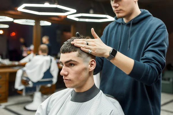 Einfach perfekt. Professioneller Friseur, der einem jungen und gutaussehenden Mann während seiner Arbeit im modernen Friseursalon die Haare stylt. Selektiver Fokus — Stockfoto