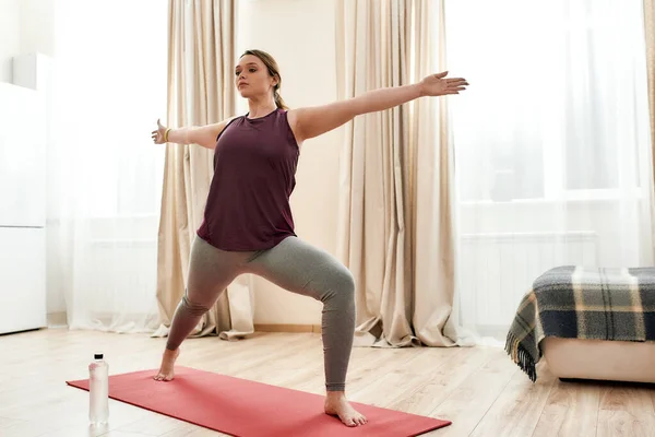 Yoga dünyasına katıl. Spor giyimli, Warriror II 'de yoga minderinin üstünde duran kıvrımlı bir kadının uzun pozu. — Stok fotoğraf