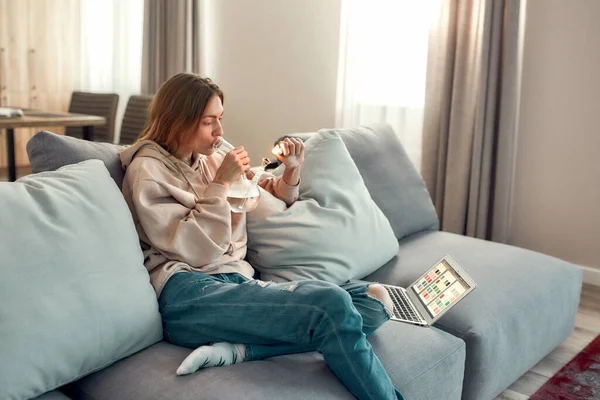 Gestión del estrés. Mujer caucásica joven sentada en el sofá en casa y encendiendo cannabis en el recipiente de la pipa de agua de vidrio o bong. Concepto de legalización del cannabis y las malas hierbas — Foto de Stock