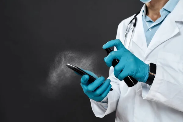 Tisztítsd meg a telefonod. Vágott fénykép férfi orvos orvosi egyenruhában és kék steril kesztyű fertőtlenítő mobil telefon fertőtlenítő spray — Stock Fotó