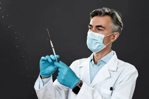검은 배경에 맞서서 독감, 코로나 바이러스 (coronavirus), 코로나 바이러스 (covid-19) 를 주사 한 혐의로 의료 유니폼을 입고 보호 마스크 주사기를 착용하고 있는 성숙 한 남성 의사 — 스톡 사진