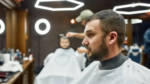 Sakal düzeltme. Berber dükkanında oturan yakışıklı ve sakallı bir adamın yan görüntüsü. — Stok fotoğraf