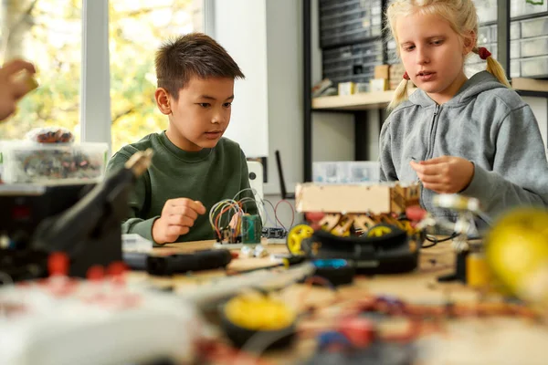 Junge Generation. Asiatische Jungen und kaukasische Mädchen bauen ihre eigenen Fahrzeuge in einem Stammrobotikkurs. Erfindungen und Kreativität für Kinder. — Stockfoto