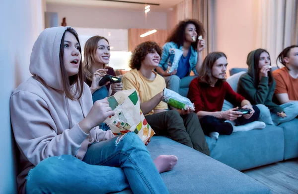 Having fun at home. Young multicultural people playing video games, eating snacks and relaxing together on the couch at home. Friends spending time together — Stock Photo, Image