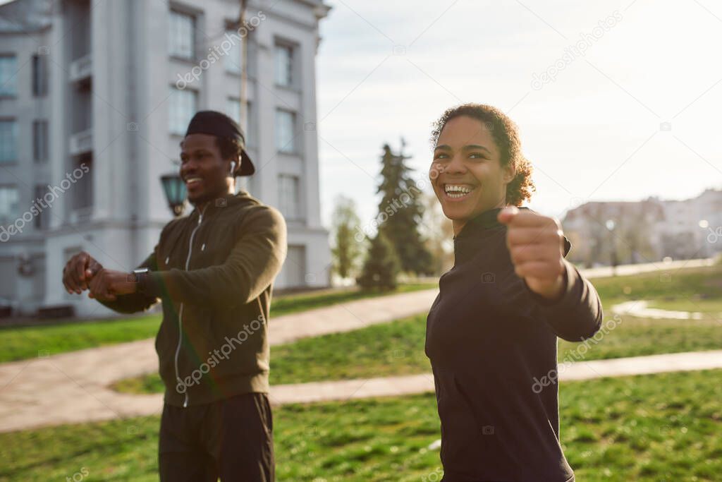 Sporty and happy african couple exercising in the morning outdoors and smiling. Positive dark skinned man and woman in black sportswear working out in park