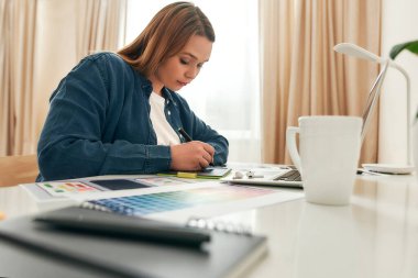 Evden çalışan kadın tasarımcı. Evde yaratıcı iş yerinde otururken, günlük kıyafetleriyle grafik tabletine bir şeyler çizen genç yaratıcı kadın.