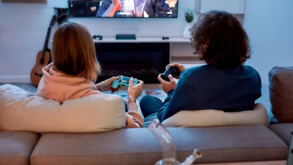 Visão traseira do jovem casal jogando videogames depois de fumar maconha de um cachimbo enquanto estava sentado no sofá em casa — Fotografia de Stock