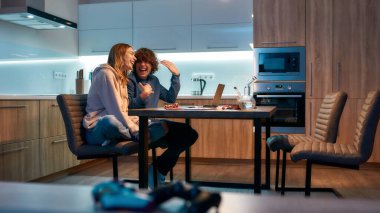 Mutlu çift evde mutfakta otururken marihuana içtikten sonra gülüp eğleniyor. Marihuana aletleri masada.