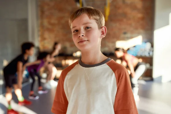 Sé fuerte. Retrato de un niño sonriendo a la cámara antes de calentarse, haciendo ejercicio junto con otros niños y entrenando en el gimnasio. Deporte, estilo de vida saludable, concepto de infancia activa —  Fotos de Stock