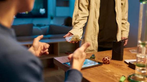 Young man buying marijuana. Cropped photo of drug trafficker holding bag of weed or cannabis at clients home