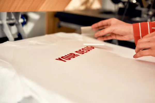 We bring print to life. Cropped shot of hand of woman removing the backing from advertisement sticker with text while putting it on a T-Shirt — Stock Photo, Image