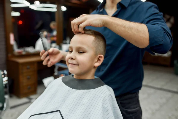 Piccolo uomo. Ragazzo carino seduto su una sedia da barbiere e sorridente mentre il barbiere maschile si acconciava i capelli. Barbiere — Foto Stock