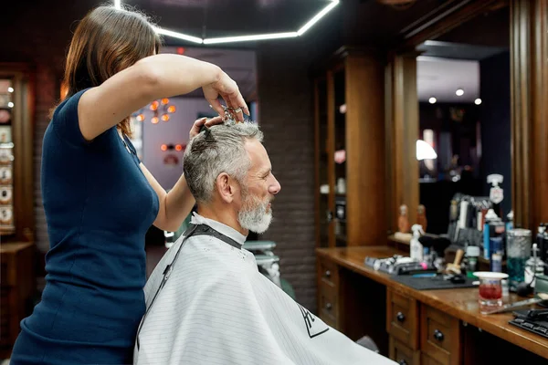 Uomo maturo in visita parrucchiere. Vista laterale di barbiere professionista che fa taglio di capelli per un elegante uomo di mezza età seduto in poltrona davanti allo specchio — Foto Stock