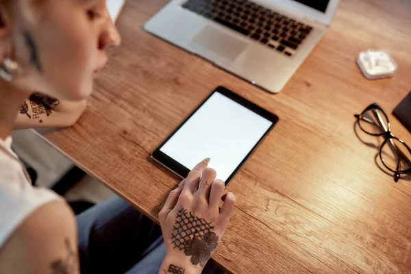 Comprobación de horarios. Mujer joven tatuada con corte de pelo corto usando tableta digital mientras está sentada en su lugar de trabajo. Mujer de negocios en el trabajo — Foto de Stock