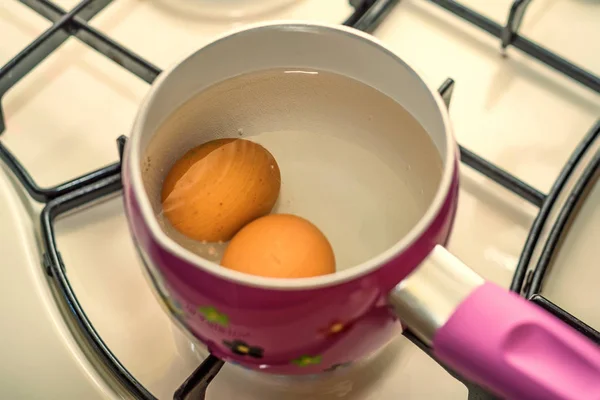 Кипячение двух яиц в воде в кастрюле из нержавеющей стали — стоковое фото