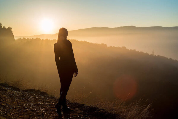 Female hiker standing on edge of rock at sunrise