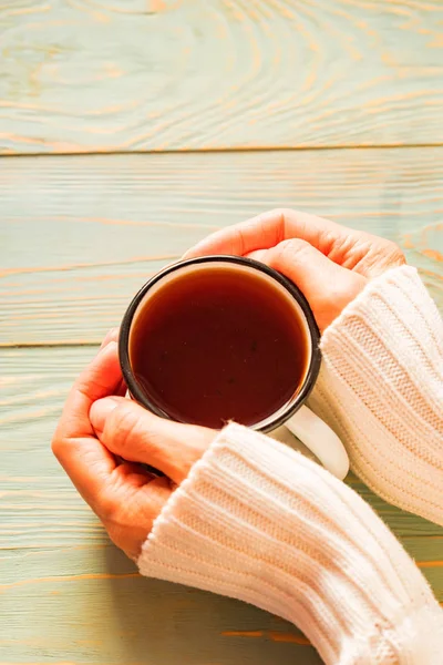 Woman in sweater holds cup of tea on wooden table — Stock Photo, Image