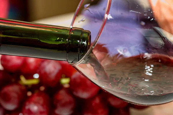 Pouring red wine into the glass against grape — Stock Photo, Image