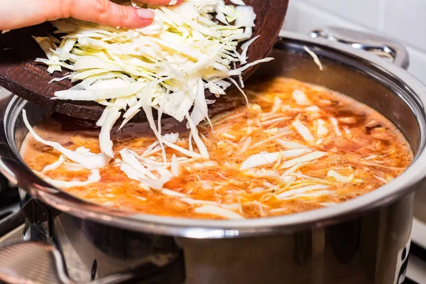 Female hands add chopped cabbage to soup — Stock Photo, Image