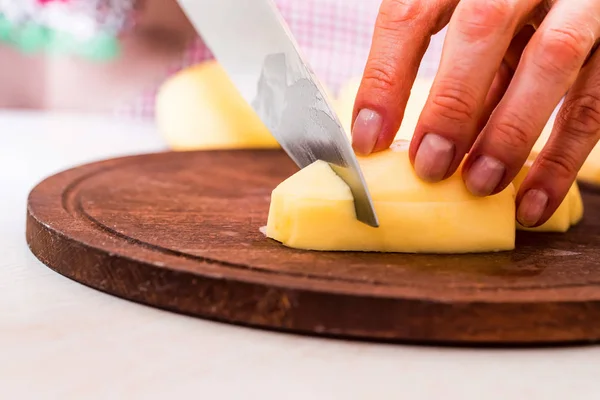 Female hands cut potatoes on wooden board — Stock Photo, Image