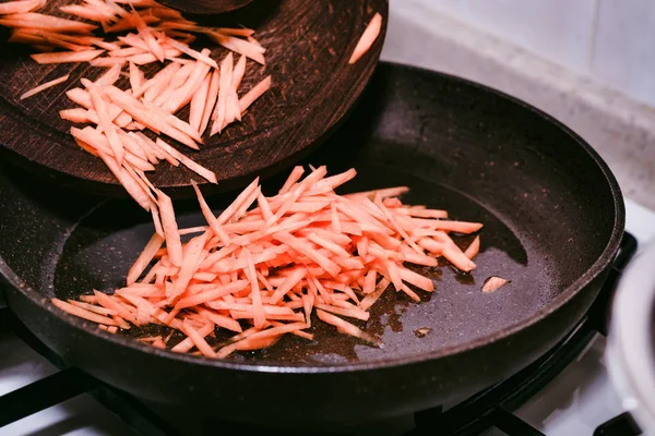 Female hands add chopped carrot to frying pan — Stock Photo, Image