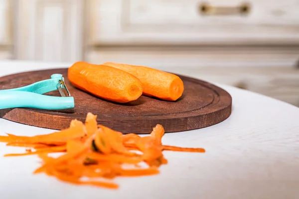 Peeled carrots and their peel on wooden board — Stock Photo, Image