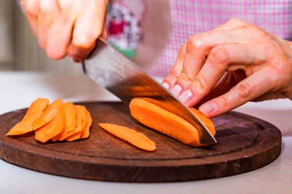 Womans hands slice carrot on wooden board — Stock Photo, Image
