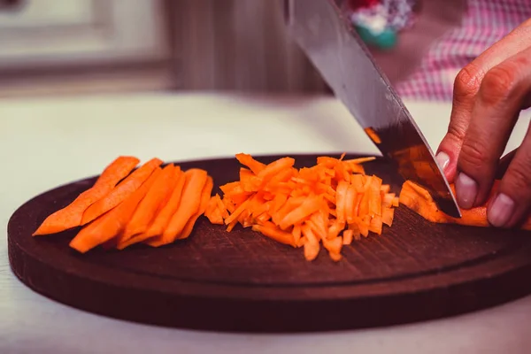 Womans hands slice carrot on wooden board — Stock Photo, Image