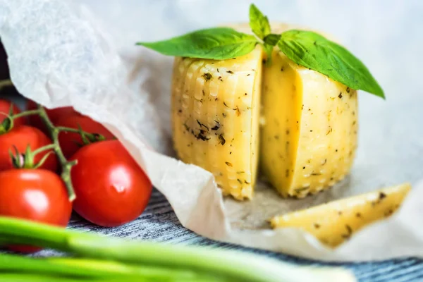 Rustic cheese with herbs on paper and vegetables — Stock Photo, Image