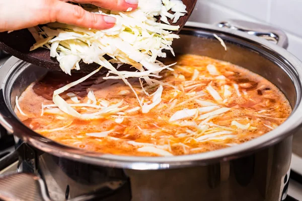 Руки женщины добавляют нарезанную капусту в суп — стоковое фото