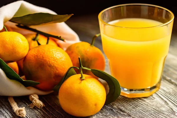 Стакан свежего сока и мандаринов на столе — стоковое фото