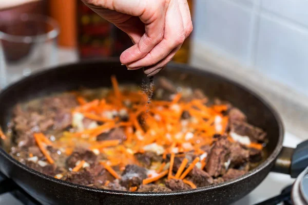 Hand adds salt to beef stew close — Stock Photo, Image