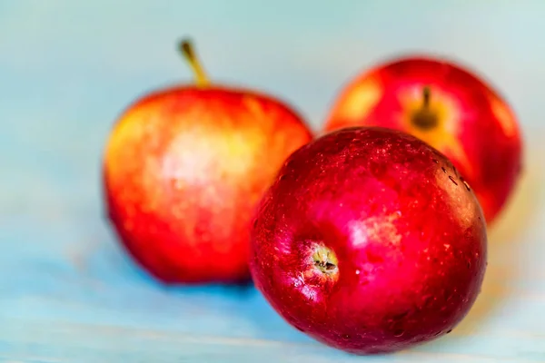 Tres manzanas rojas enteras en la superficie de madera azul — Foto de Stock