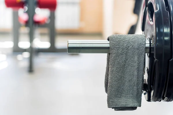 Grey towel hangs on barbell in gym — Stock Photo, Image