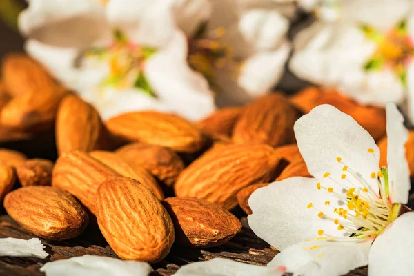 Almonds and white flowers on dark wooden surface