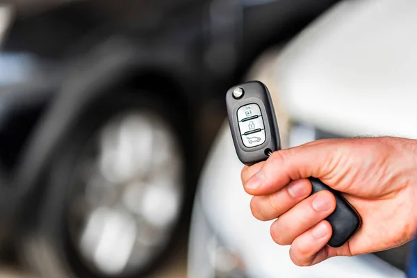 La mano masculina sostiene la llave del coche en sala de exposición del coche — Foto de Stock