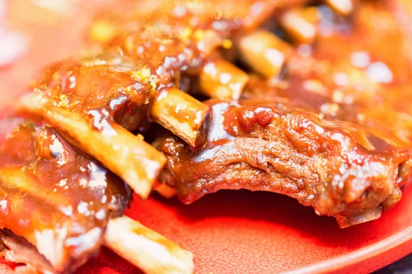 Close up roasted pork ribs in orange sauce served on red plate — Stock Photo, Image