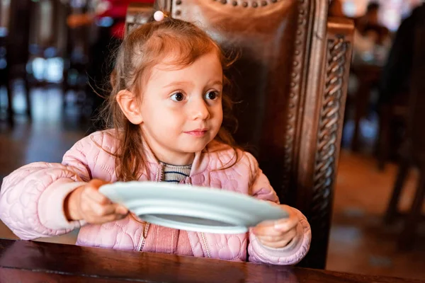 Menina pré-escolar bonito pede comida com prato vazio nas mãos — Fotografia de Stock